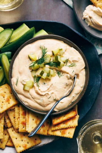 overhead view of a bowl of dill pickle dip surrounded by crackers and cut vegetables