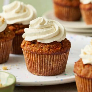 carrot cake cupcakes arranged in a scene with a green background, topped with white cream cheese frosting