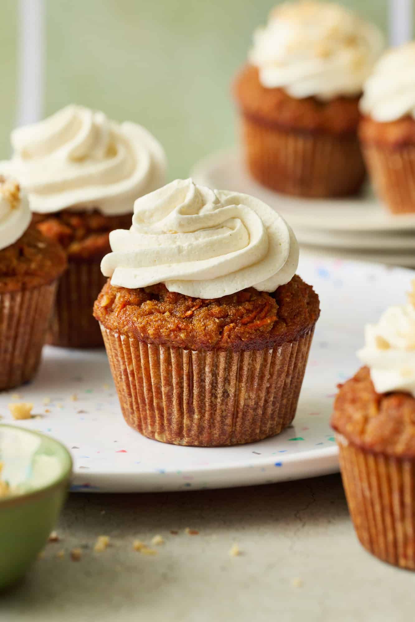 carrot cake cupcake with cream cheese frosting on a white speckled plate