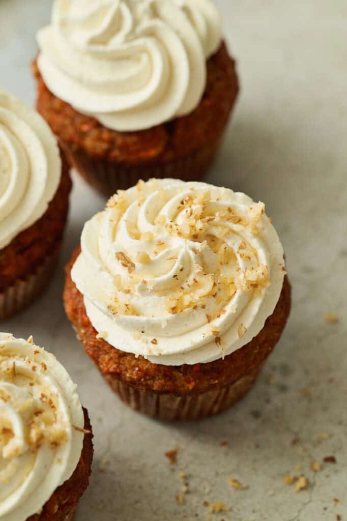 closeup of a carrot cake cupcake with frosting piped on top and walnuts sprinkled on top