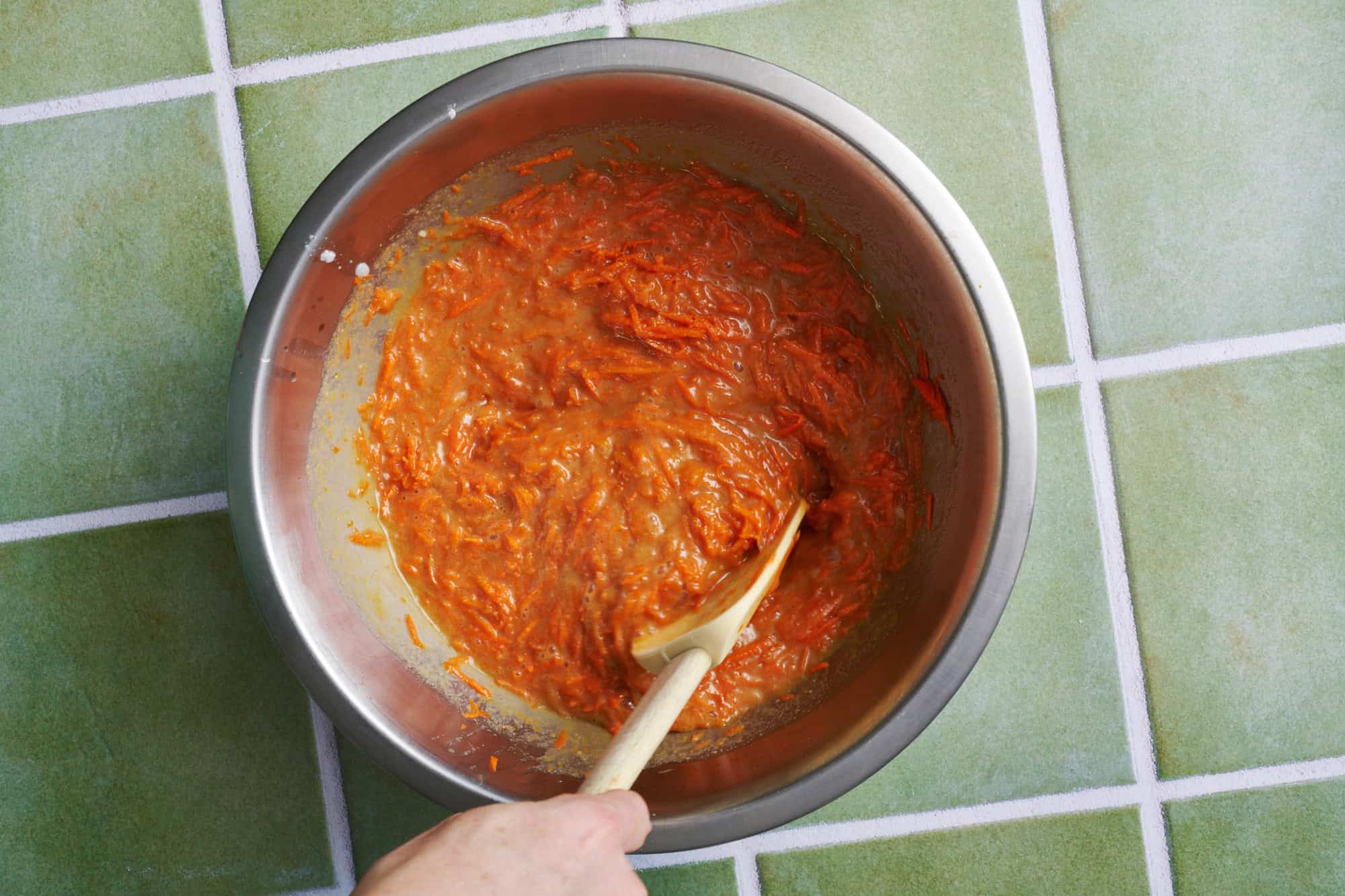 folding shredded carrots into the batter in a metal bowl