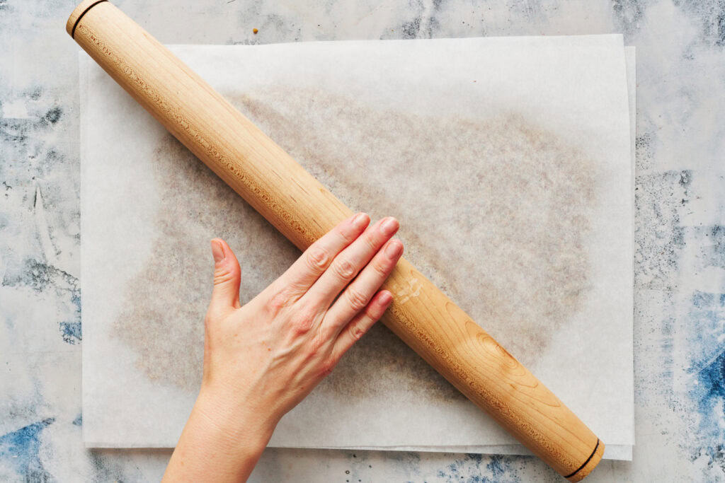 rolling out the dough between two pieces of parchment paper with a rolling pin