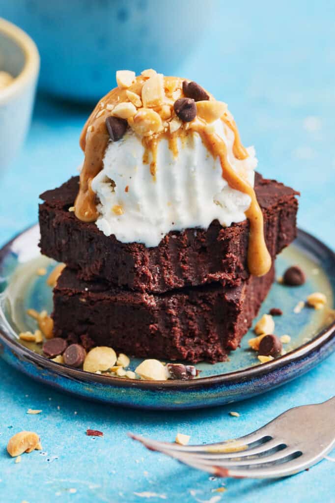 a brownie sundae topped with coconut ice cream, peanut butter and chocolate chips