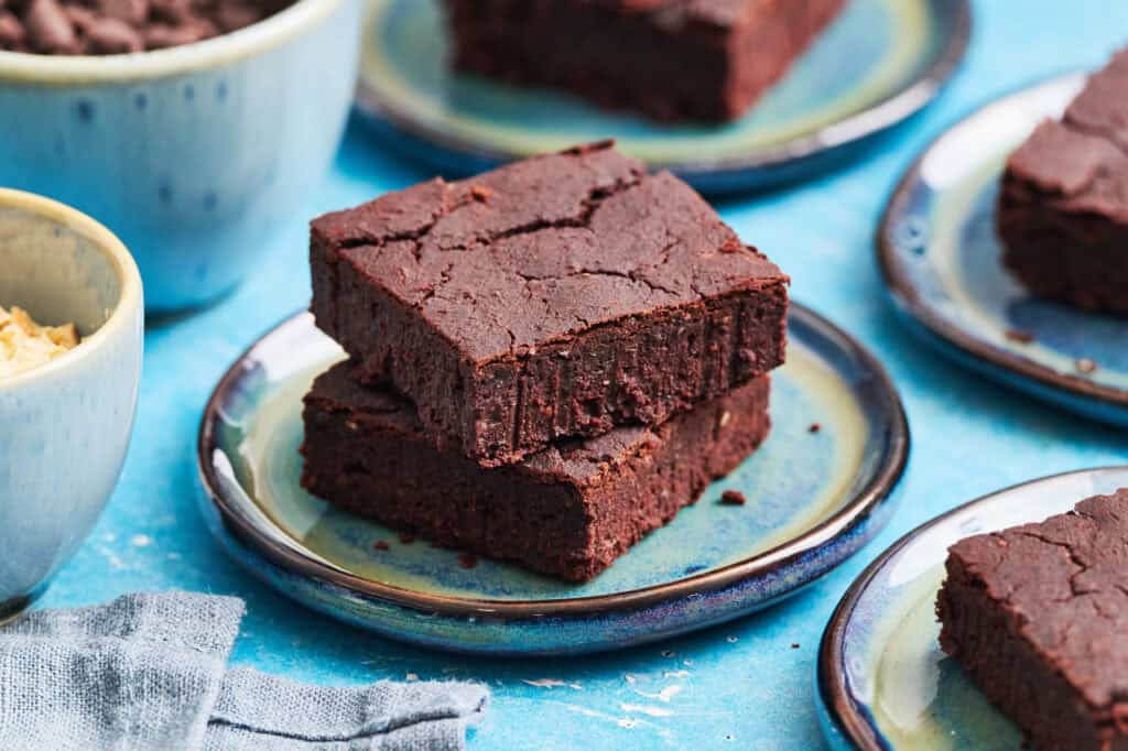 two gluten free sugar free brownies on a small dessert plate in a scene with a blue background