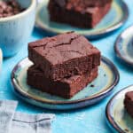 two brownies stacked on a blue plate with other brownies around the scene