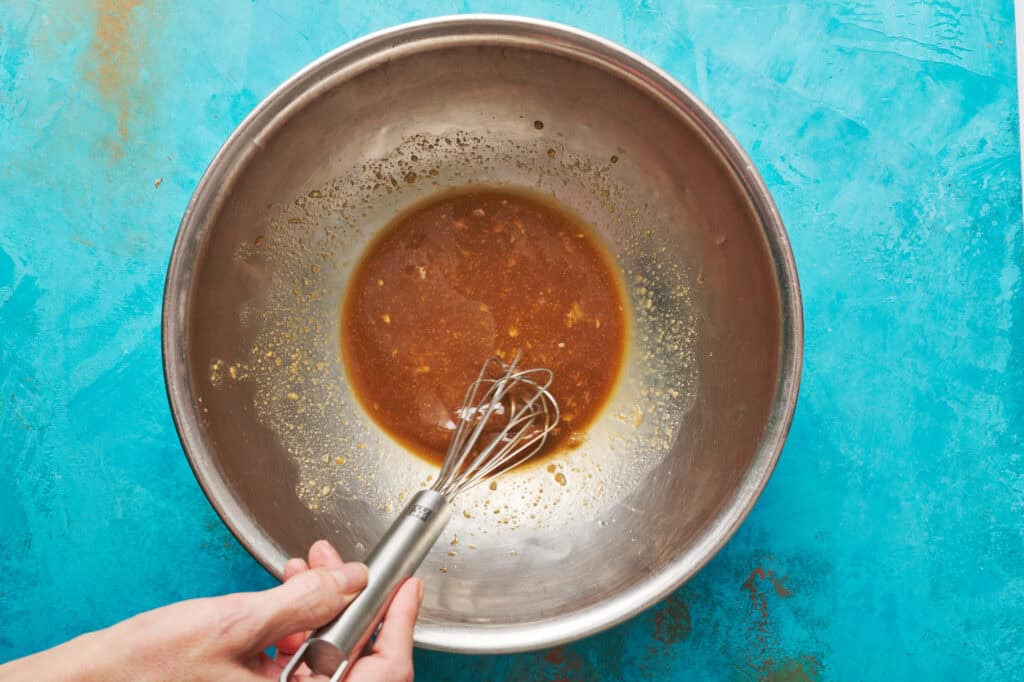 a hand using a whisk to combine the marinade ingredients