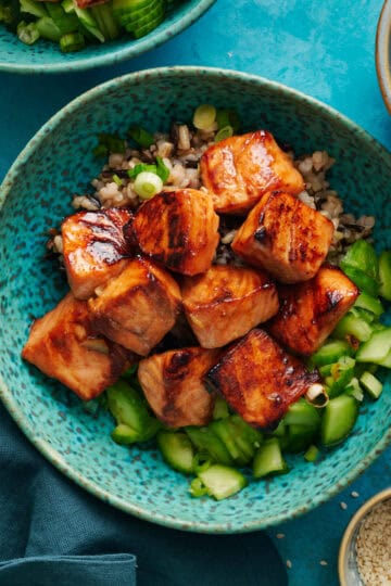 Overhead of miso glazed salmon bites over a bed of quinoa and cucumers.