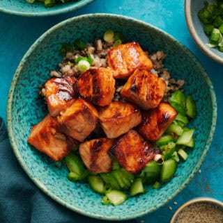 Overhead of miso glazed salmon bites over a bed of quinoa and cucumers.