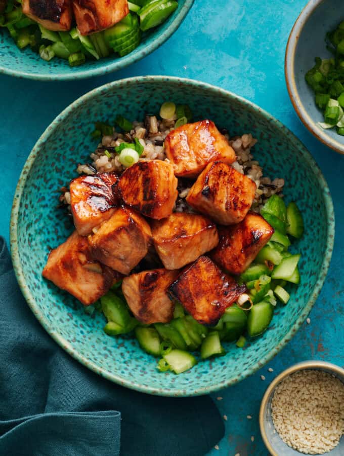 Overhead of miso glazed salmon bites over a bed of quinoa and cucumers.