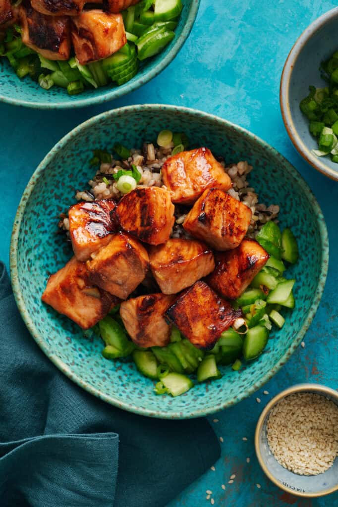 Overhead of miso glazed salmon bites over a bed of quinoa and cucumers.