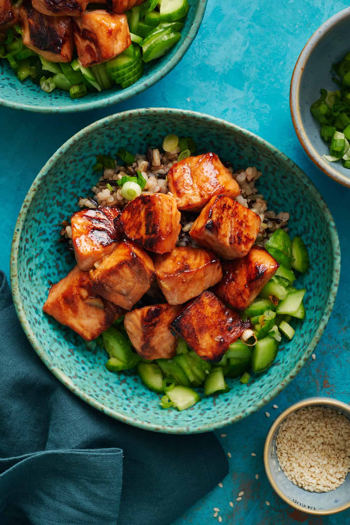 Overhead of miso glazed salmon bites over a bed of quinoa and cucumers.