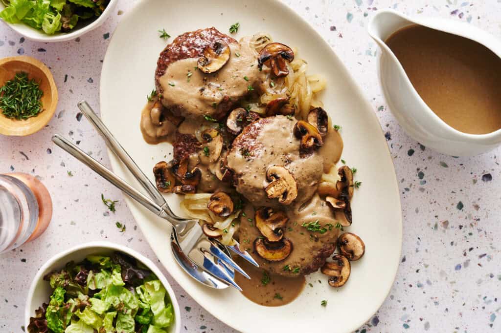 overhead view of a platter with four hamburger steaks smothered in gravy with onions and mushrooms