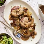 Overhead view of a platter with Oven Hamburger Steaks smothered in mushroom gravy with onions and mushrooms scattered around.