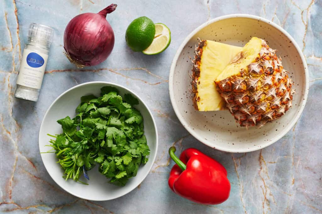 ingredients for pineapple pico de gallo including cilantro, red bell pepper, lime, pineapple, red onion and salt