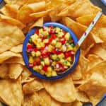 Closeup view of a platter of tortilla chips with pineapple pico de gallo in the center with a spoon.