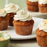 carrot cake cupcakes arranged in a scene with a green background, topped with white cream cheese frosting