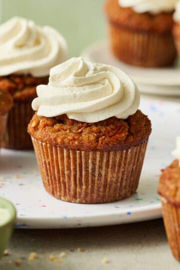 carrot cake cupcakes arranged in a scene with a green background, topped with white cream cheese frosting