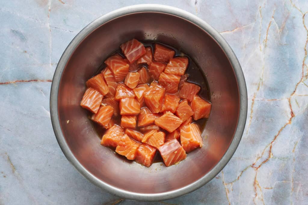 fresh salmon cut into smaller pieces in a metal bowl with the marinade