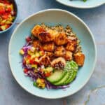 Overhead view of a bowl filled with salmon bites with avocado and pineapple salsa, along with a side of rice