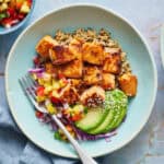 overhead of teriyaki salmon bites in a bowl with quinoa rice, avocado, salsa and cabbage with sesame seeds on the the side