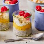 a glass jar with pineapple chia seed pudding topped with coconut and raspberries