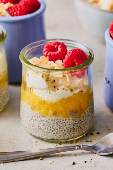 a glass jar with pineapple chia seed pudding topped with coconut and raspberries