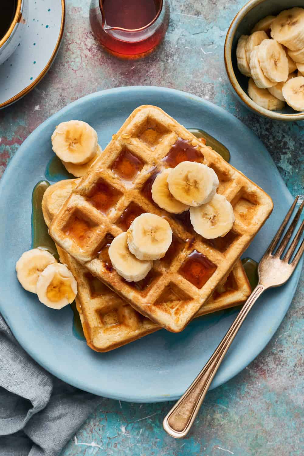 banana protein waffles with sliced bananas and syrup on a plate with sliced bananas on the side