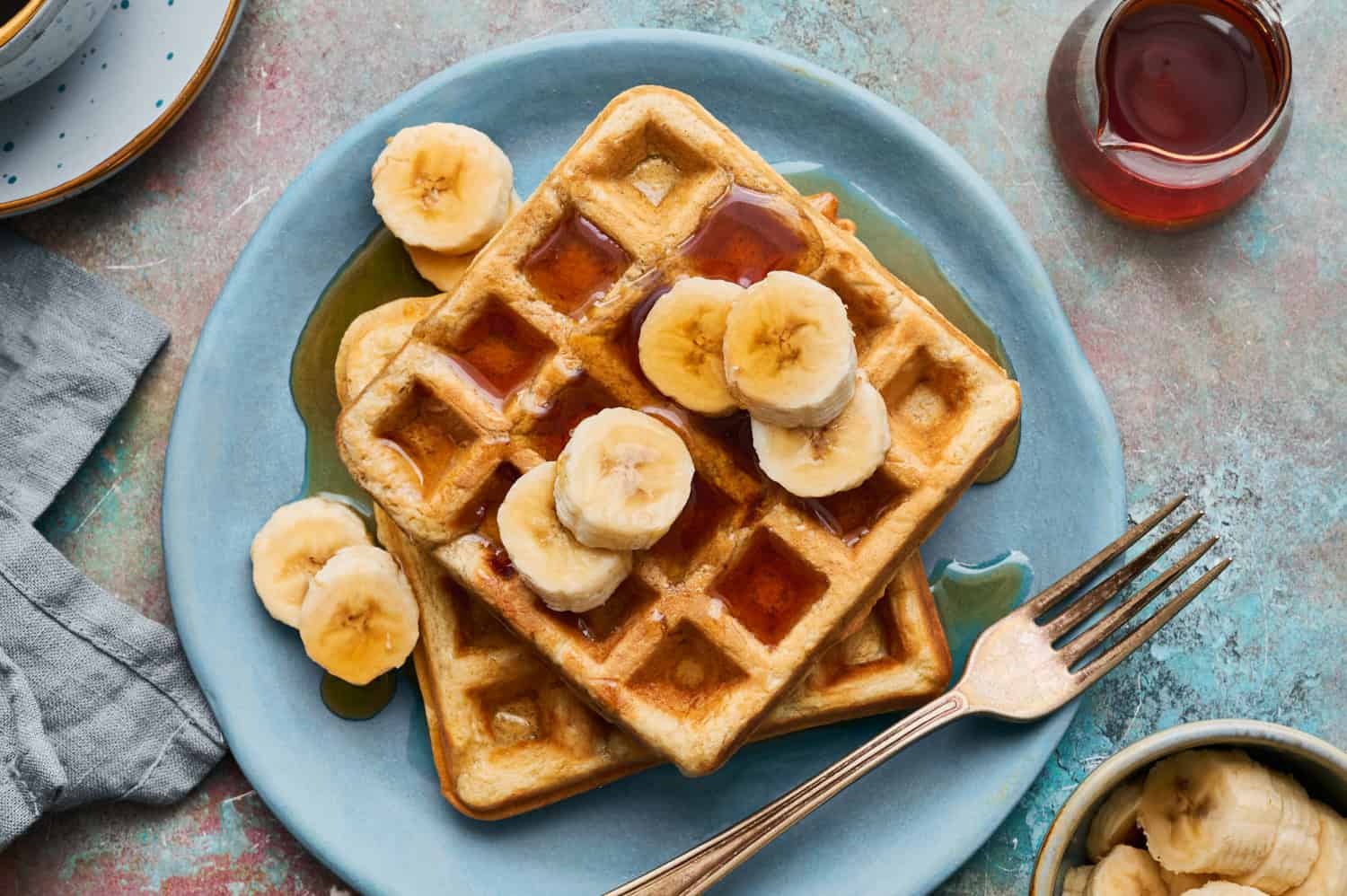 banana protein waffles with sliced bananas and syrup on a plate with sliced bananas on the side