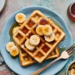 banana protein waffles with sliced bananas and syrup on a plate with sliced bananas on the side