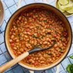 a white pot filled with vegan charro beans with a ladle scooping out some beans with tomato and spices