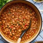 a white pot filled with vegan charro beans with a ladle scooping out some beans with tomato and spices