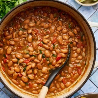 a white pot filled with vegan charro beans with a ladle scooping out some beans with tomato and spices