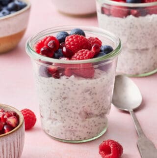 chia yogurt parfaits on a pink background with fresh raspberries, blueberries and pomegranate seeds surrounding