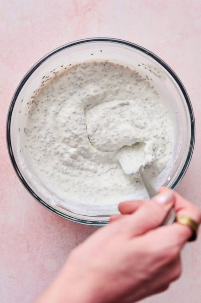 A bowl with a hand stirring together the yogurt, chia seeds and almond milk.