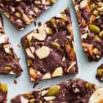 overhead view of chocolate bark with sea salt, almonds, pumpkin seeds and dates cut up on a blue surface