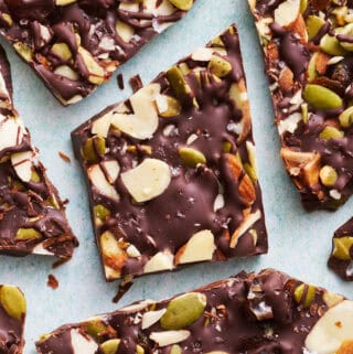 overhead view of chocolate bark with sea salt, almonds, pumpkin seeds and dates cut up on a blue surface