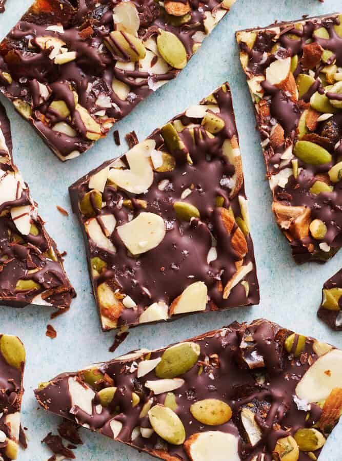 overhead view of chocolate bark with sea salt, almonds, pumpkin seeds and dates cut up on a blue surface