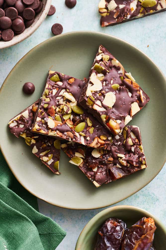 overhead view of chocolate bark with sea salt, almonds, pumpkin seeds and dates on a plate