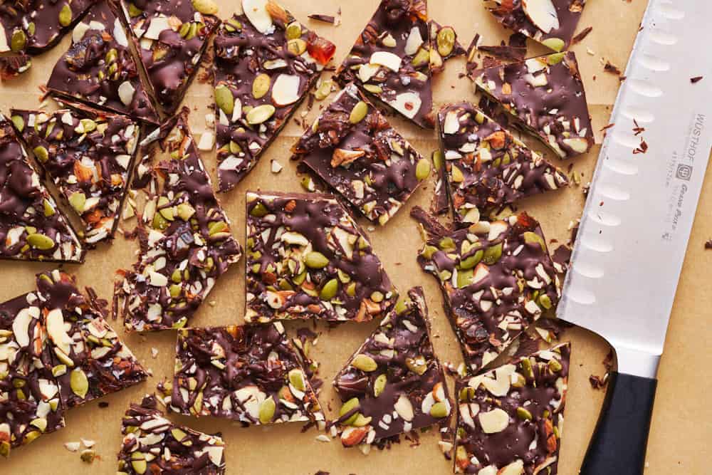 overhead view of chocolate bark with sea salt, almonds, pumpkin seeds and dates chopped on a surface