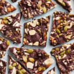 overhead view of chocolate bark with sea salt, almonds, pumpkin seeds and dates cut up on a blue surface