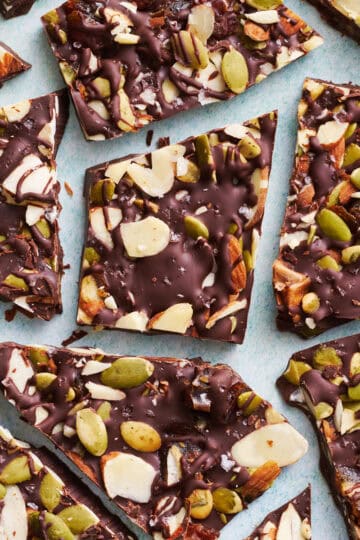 overhead view of chocolate bark with sea salt, almonds, pumpkin seeds and dates cut up on a blue surface