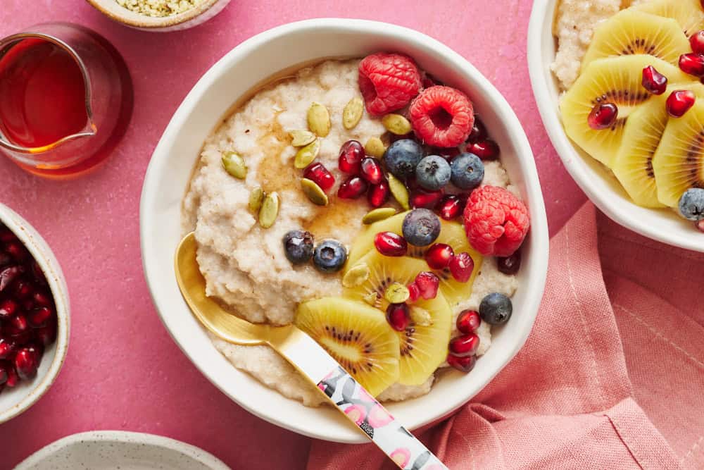 fonio porridge in a bowl topped with kiwi, raspberries, blueberries, pumpkin seeds and pomegranate