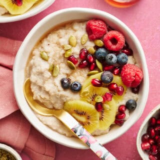 fonio porridge in a bowl topped with kiwi, raspberries, blueberries, pumpkin seeds and pomegranate