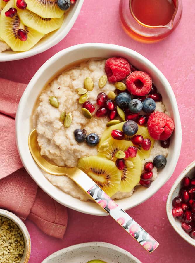 fonio porridge in a bowl topped with kiwi, raspberries, blueberries, pumpkin seeds and pomegranate