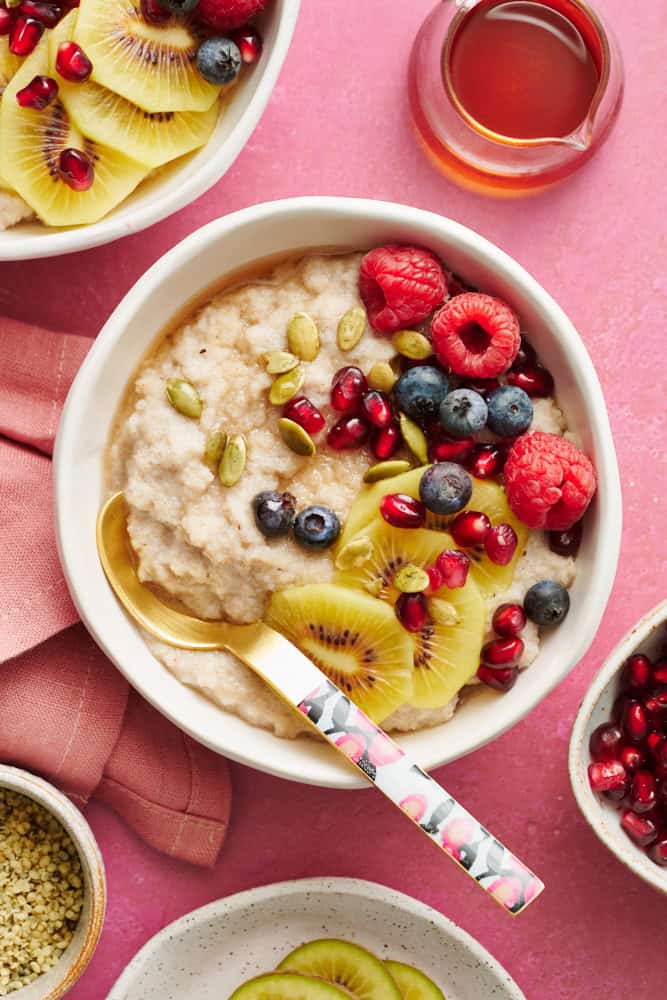 fonio porridge in a bowl topped with kiwi, raspberries, blueberries, pumpkin seeds and pomegranate