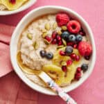 fonio porridge in a bowl topped with kiwi, raspberries, blueberries, pumpkin seeds and pomegranate