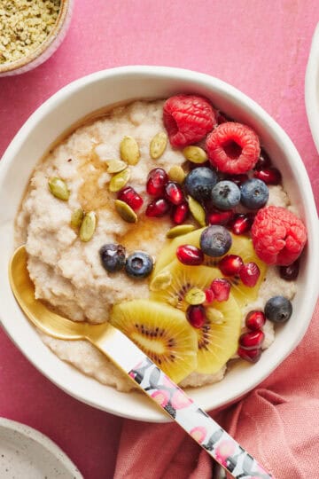 fonio porridge in a bowl topped with kiwi, raspberries, blueberries, pumpkin seeds and pomegranate