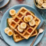 Waffles on a plate with maple syrup and sliced bananas