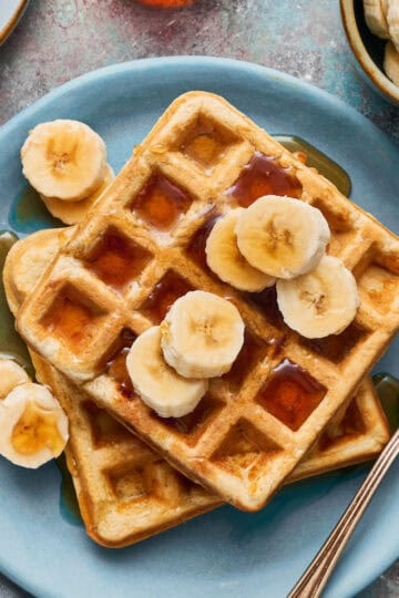 Waffles on a plate with maple syrup and sliced bananas