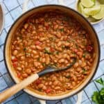 a white pot filled with vegan charro beans with a ladle scooping out some beans with tomato and spices